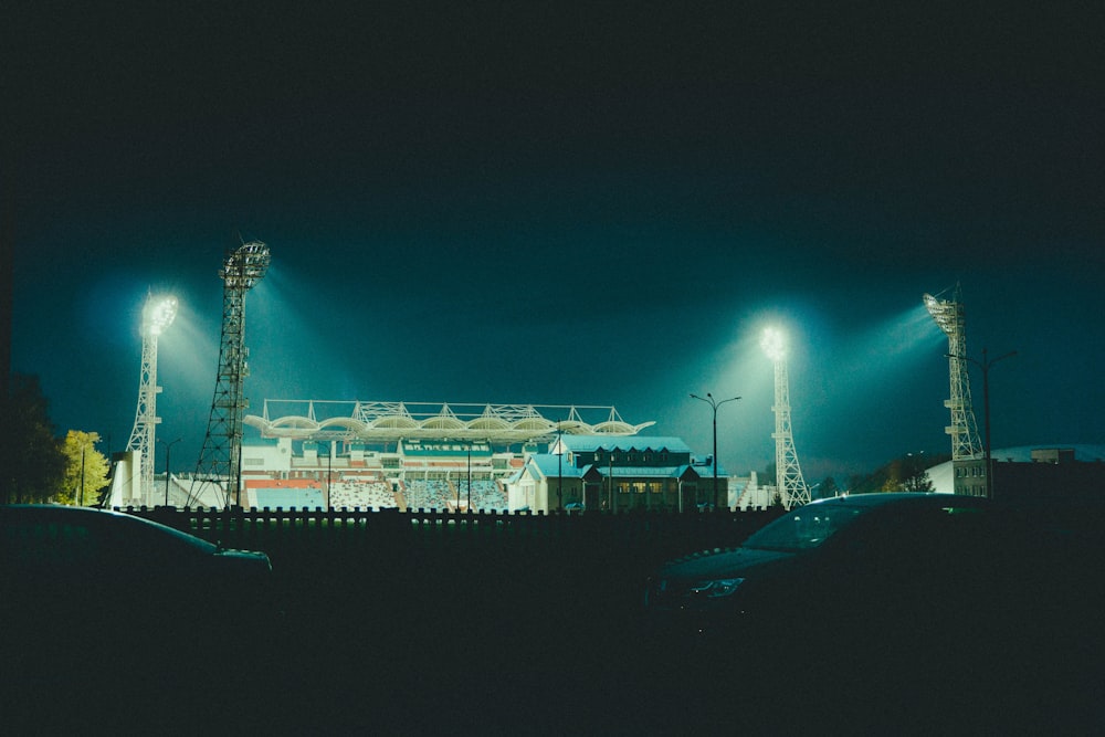 a stadium lit up at night with cars parked in front of it