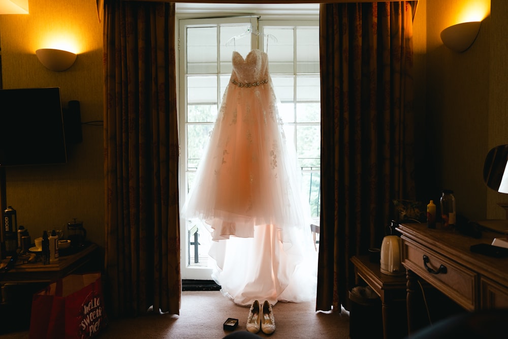 a wedding dress hanging in front of a window