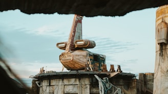 A futuristic spacecraft is perched on a circular platform amid a desert environment. The spacecraft has a weathered appearance, with a mix of beige and red colors. The sky is overcast with scattered clouds, creating a serene atmosphere.
