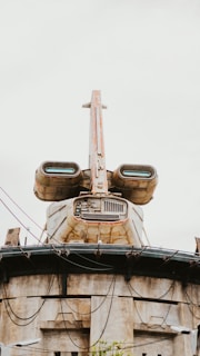 A futuristic building structure resembling a spacecraft with rust and weathered surfaces. It features large, engine-like components and intricate architectural details, with wires and cables hanging across the structure.
