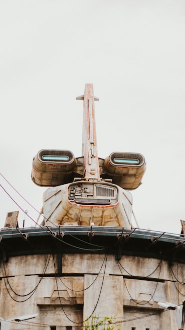 A futuristic building structure resembling a spacecraft with rust and weathered surfaces. It features large, engine-like components and intricate architectural details, with wires and cables hanging across the structure.