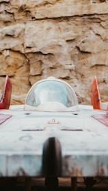 A futuristic spacecraft with a streamlined design is parked against a rocky backdrop. The spaceship has a central cockpit surrounded by a clear dome, red accents on its wings, and a weathered, metallic exterior.