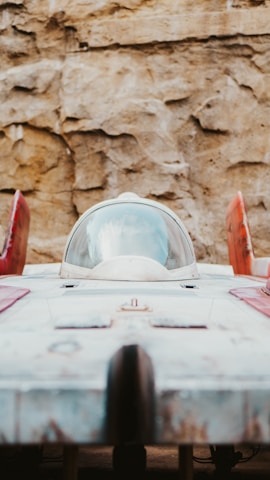 A futuristic spacecraft with a streamlined design is parked against a rocky backdrop. The spaceship has a central cockpit surrounded by a clear dome, red accents on its wings, and a weathered, metallic exterior.