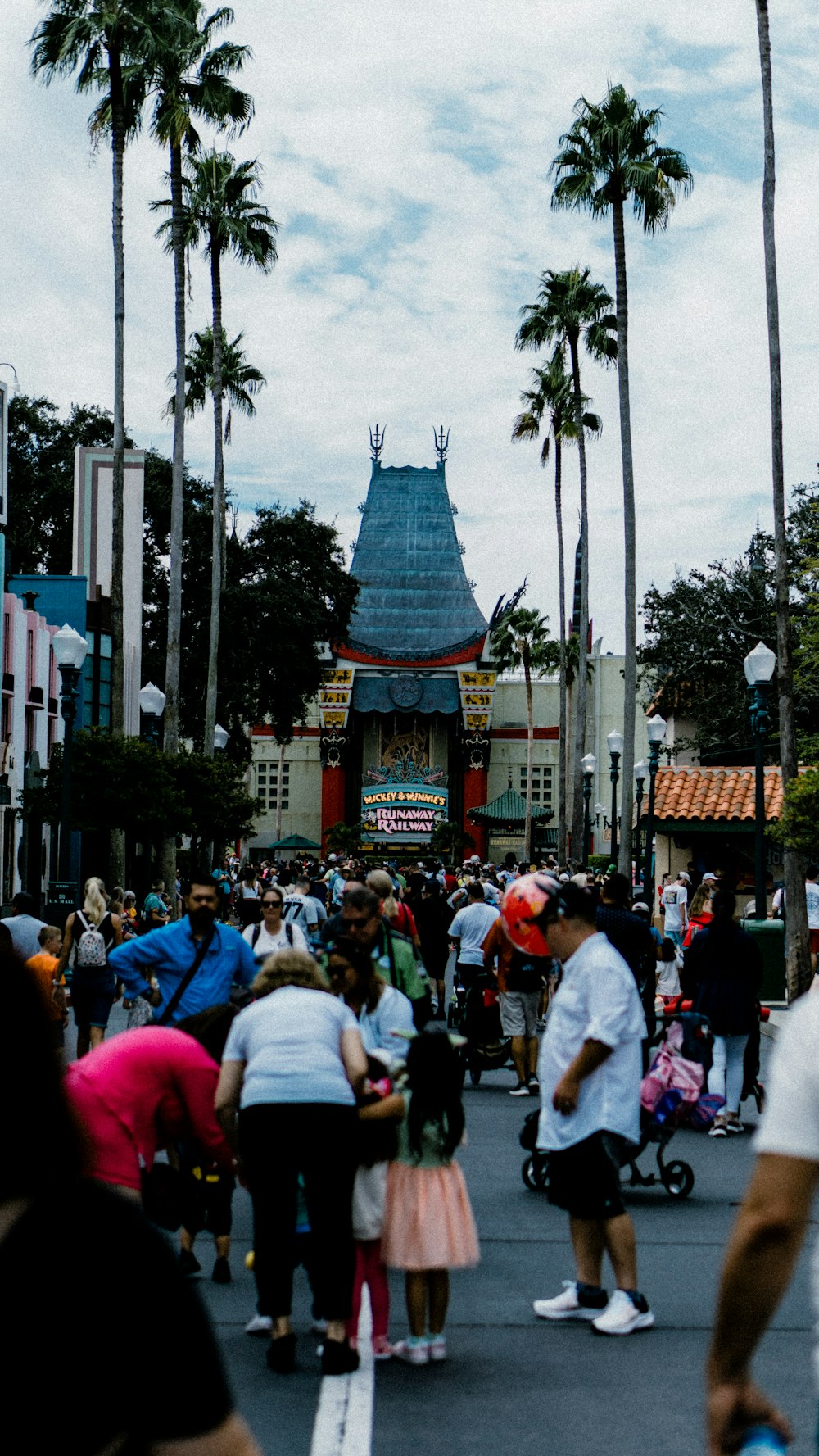 a crowd of people walking down a street next to tall palm trees