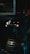 A robot with a cylindrical body and a round head featuring mechanical eyes and a red light in the center. The robot includes metallic parts and appears to be in a dimly lit industrial setting with metal bars in the background.