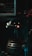 A robot with a cylindrical body and a round head featuring mechanical eyes and a red light in the center. The robot includes metallic parts and appears to be in a dimly lit industrial setting with metal bars in the background.