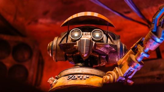 A robot with large circular eyes, a mechanical mouthpiece, and an articulated arm set against a warm, reddish background. The metal features have a worn, rustic appearance, adding a sense of vintage charm.