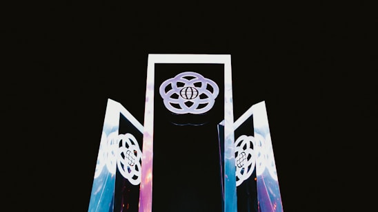 Three tall, reflective structures with geometric designs rise against a dark background. The structures display interconnected circular patterns, with a globe symbol at their center.