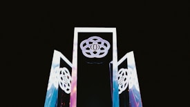 Three tall, reflective structures with geometric designs rise against a dark background. The structures display interconnected circular patterns, with a globe symbol at their center.