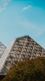 A stainless steel pyramid structure surrounded by lush greenery.