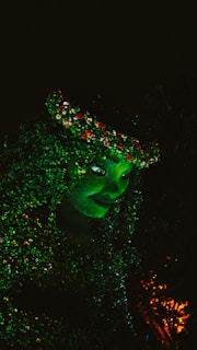 A vibrant, glowing green figure with detailed foliage and flowers intertwined throughout. The face has a peaceful and mystical expression, surrounded by lush greenery.
