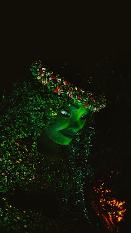 A vibrant, glowing green figure with detailed foliage and flowers intertwined throughout. The face has a peaceful and mystical expression, surrounded by lush greenery.