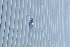 Worker repairing building facade at height with safety harness and ropes.