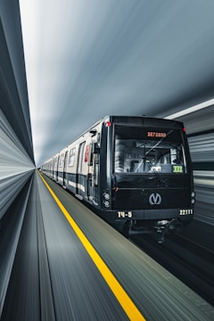A sleek, modern train is depicted moving through an underground tunnel at high speed. The train is black with some white detailing and has a digital display on the front showing the number 333. The tunnel walls are a blur, suggesting motion, and a yellow line runs along the floor next to the tracks.