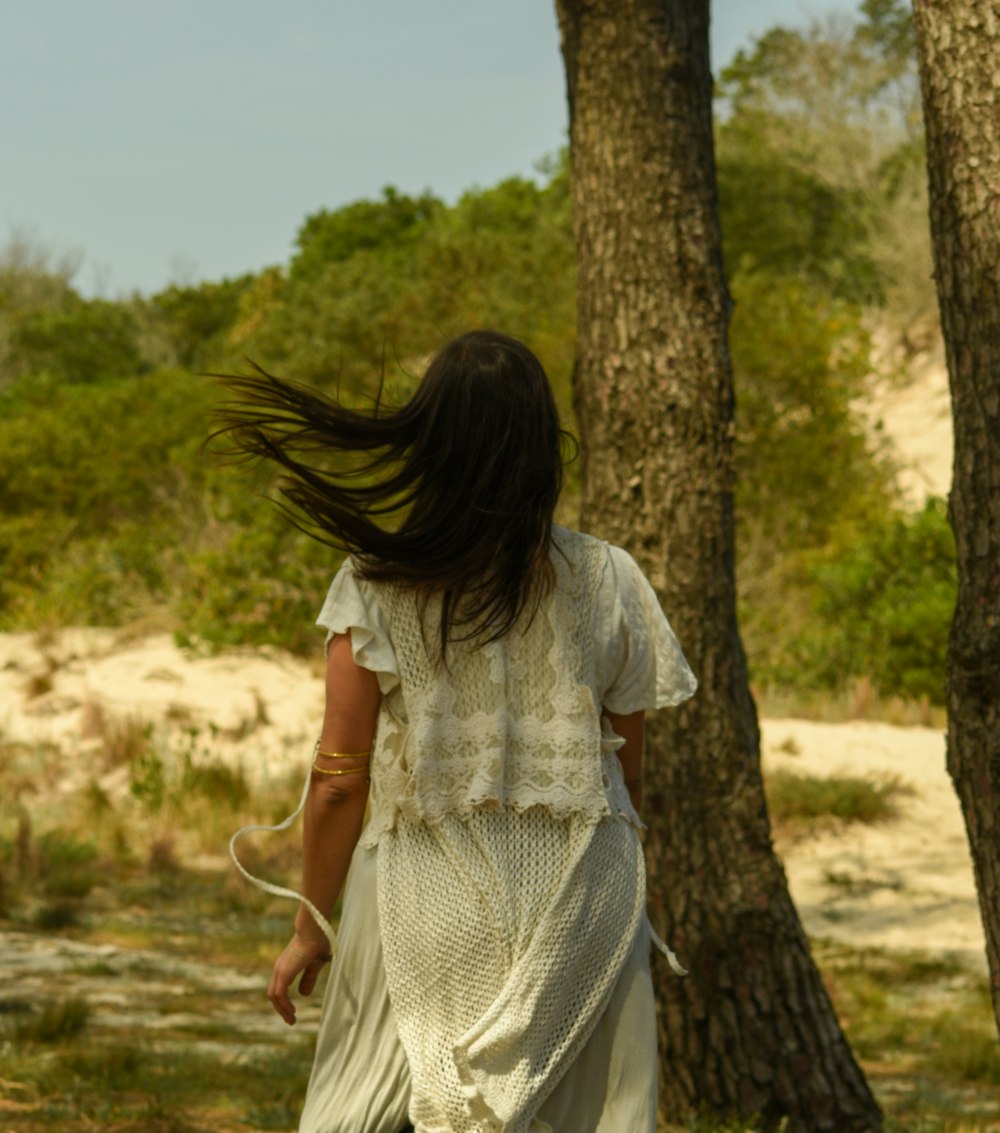 a woman in a white dress walking through a forest