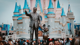 a statue of walt and mickey mouse in front of a castle