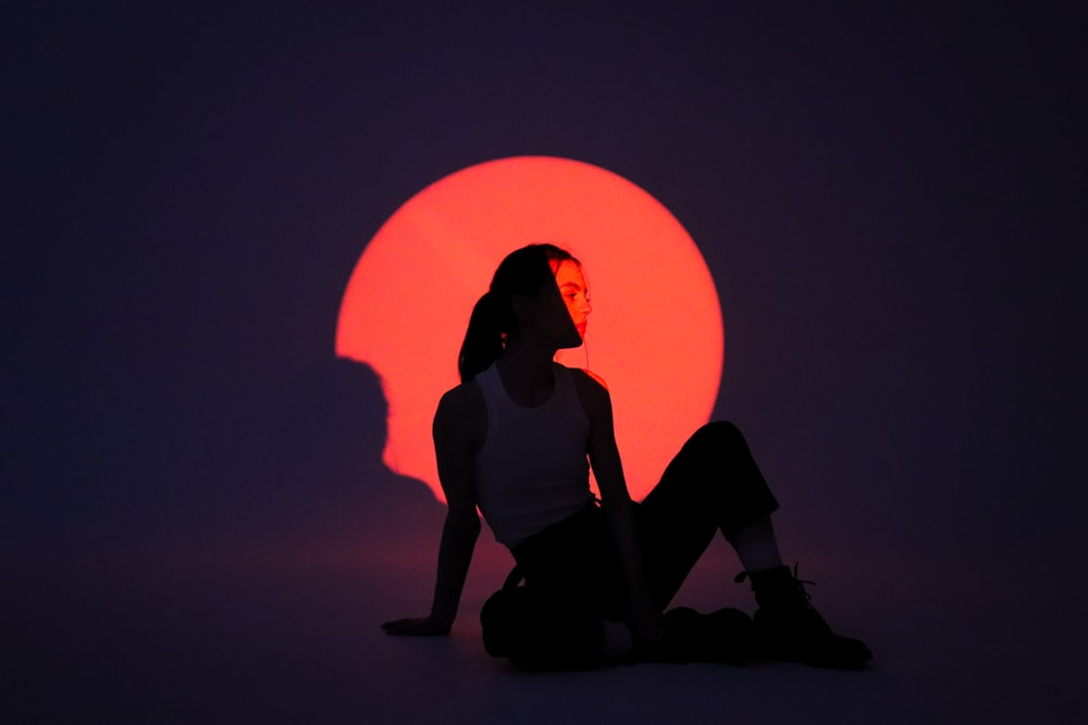 a silhouette of a woman sitting in front of a red sun