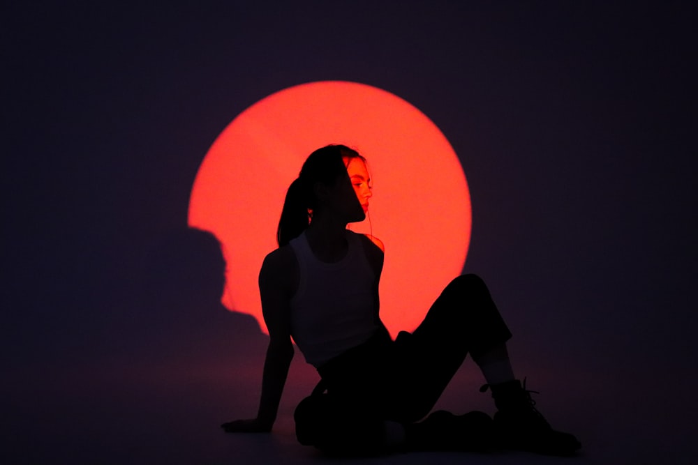 a silhouette of a woman sitting in front of a red sun