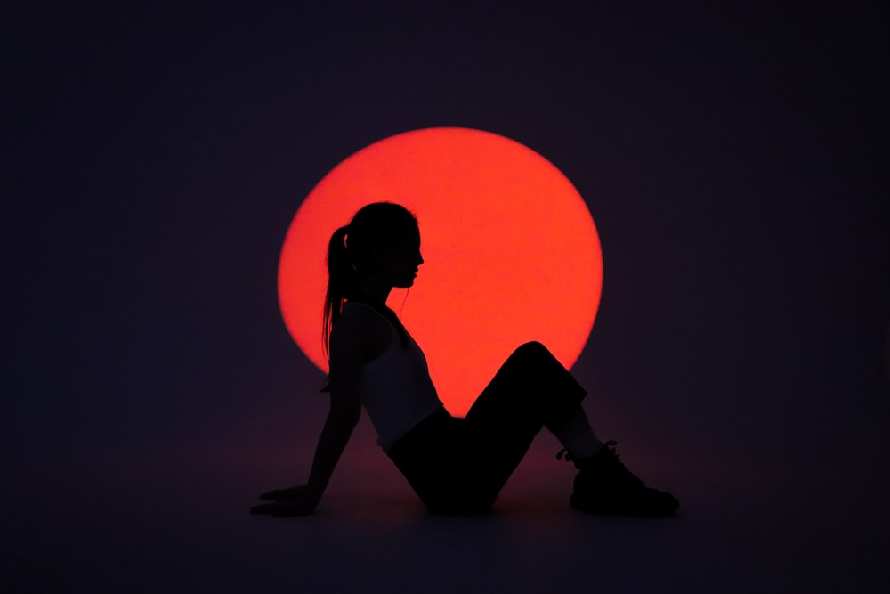 a silhouette of a woman sitting in front of a red sun