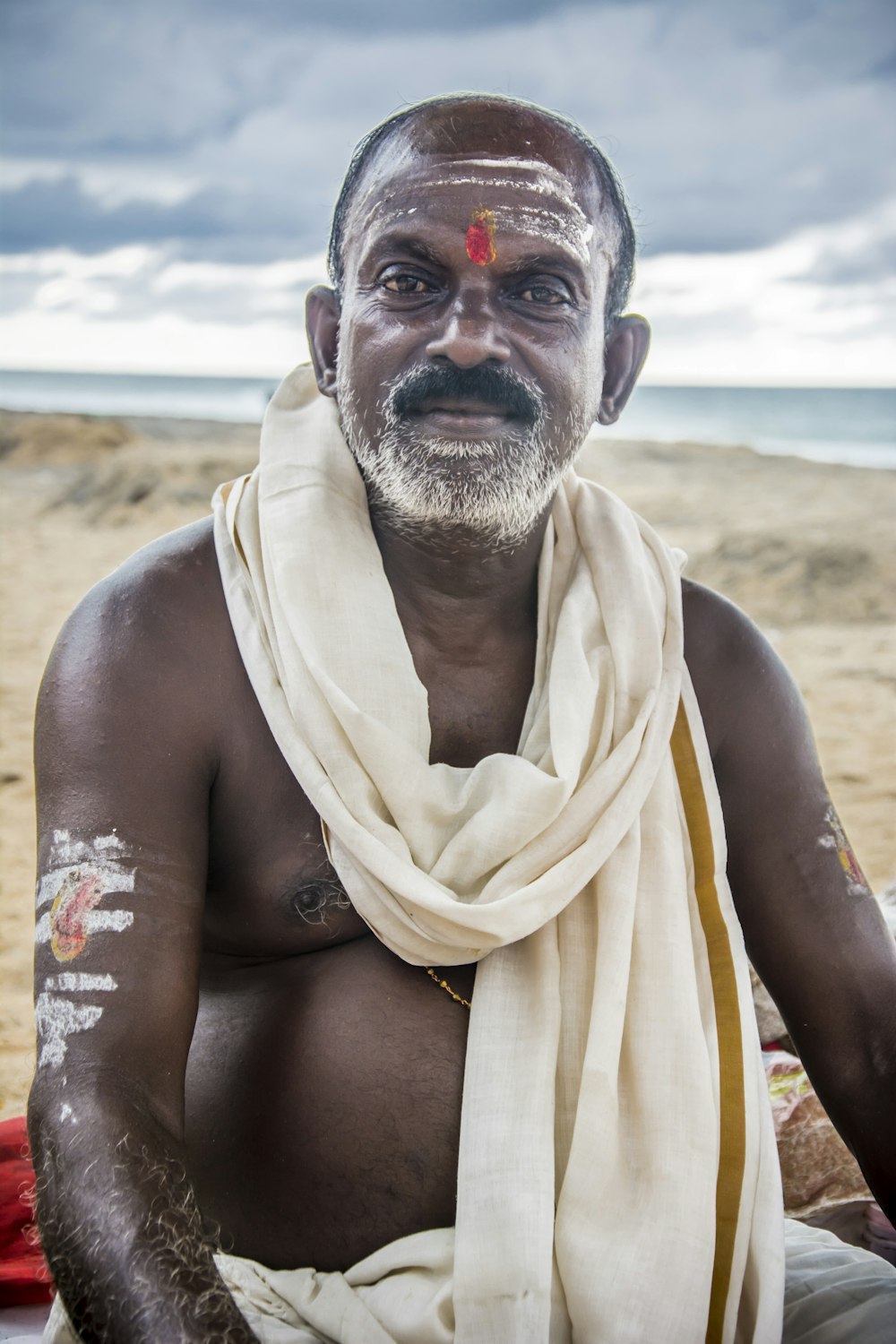 a man sitting on a beach with a white scarf around his neck