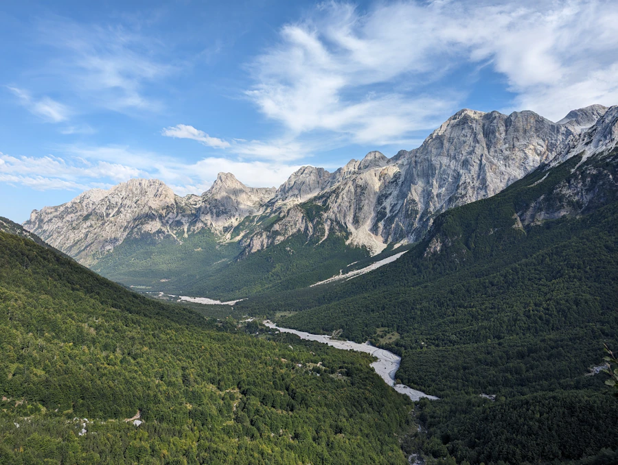 Wide river bed flowing through the Valbona valley with peaks behind