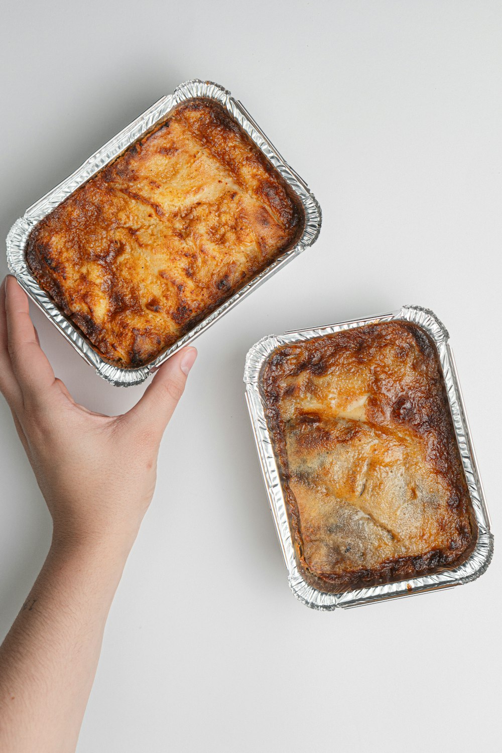 a hand holding a pan of food next to another pan of food