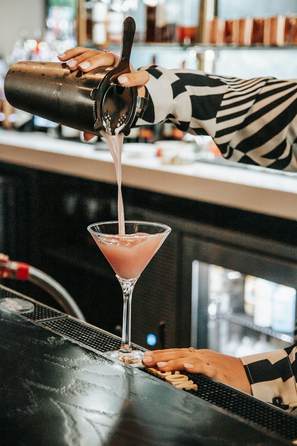 a woman pouring a drink into a martini glass