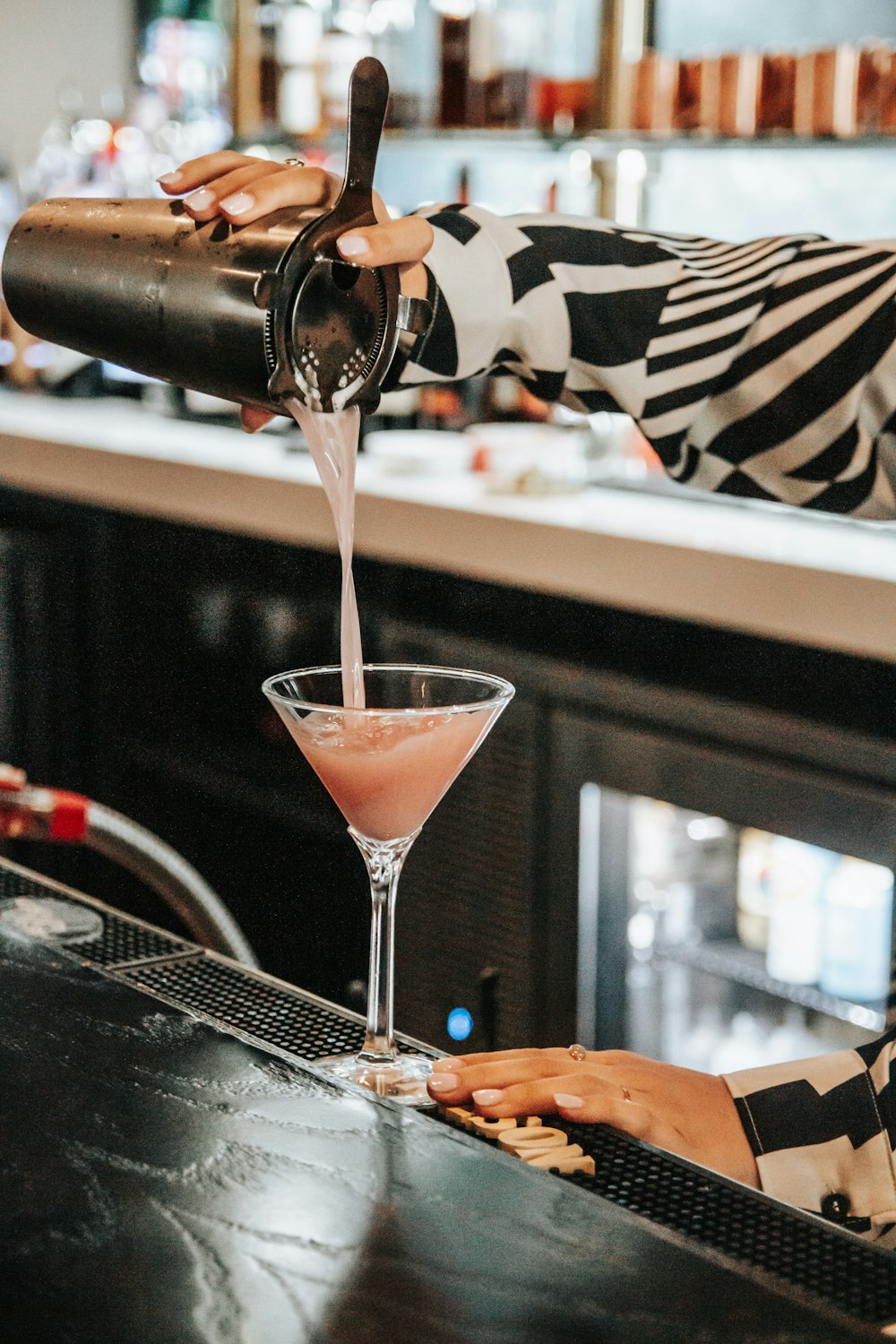 a woman pouring a drink into a martini glass