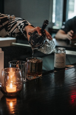 A bartender pouring a glass of golden cachaça in a cozy bar setting.