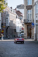 Rustic European village street with cobblestones and colorful buildings seen from the driver’s seat of a convertible