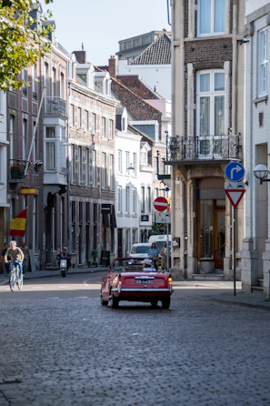 Rustic European village street with cobblestones and colorful buildings seen from the driver’s seat of a convertible