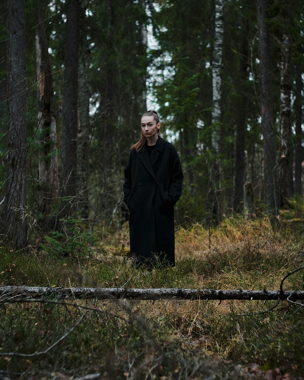 a woman in a black coat standing in a forest