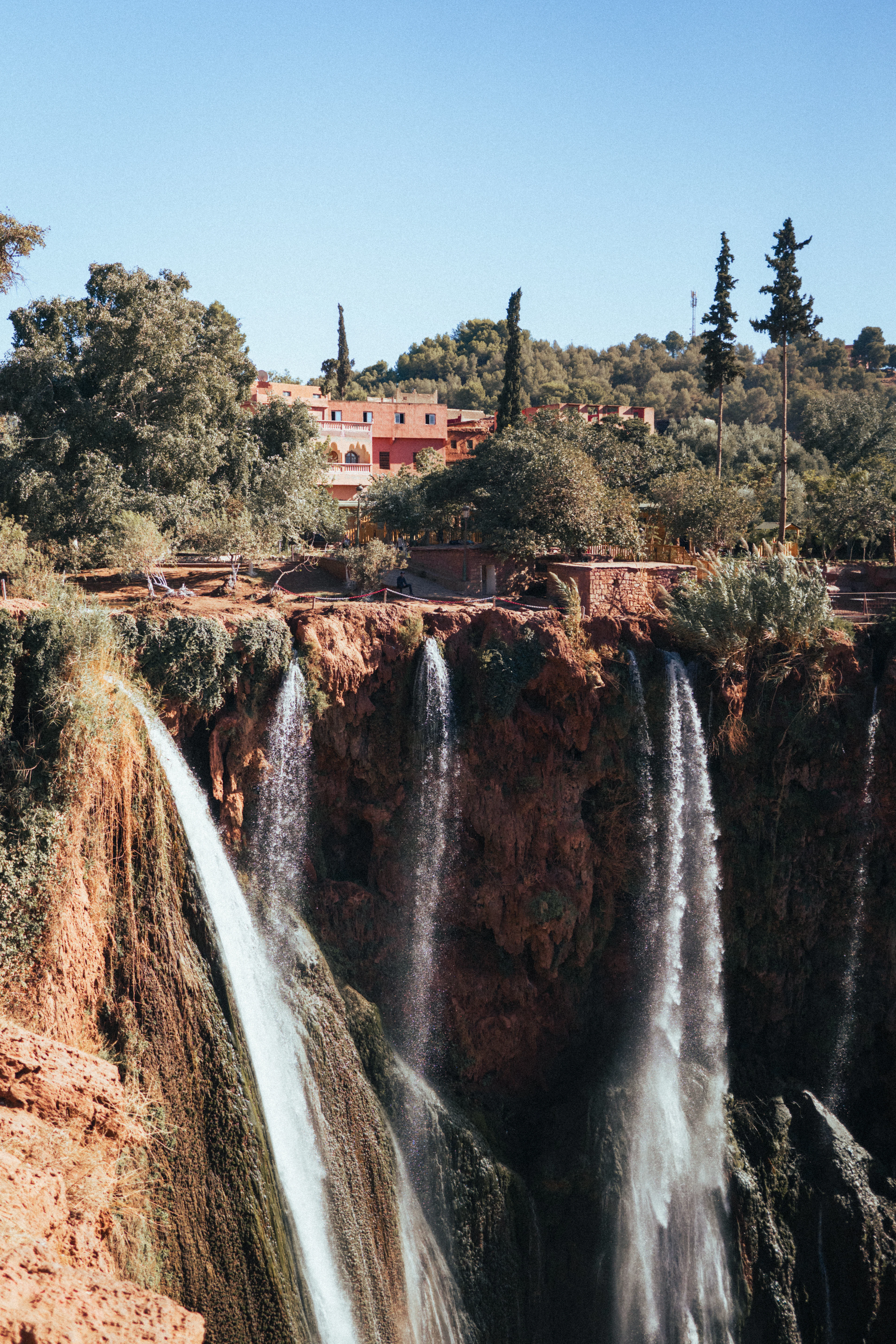 The Ouzoud waterfalls pouring down a green gorge, with a footbridge crossing above them