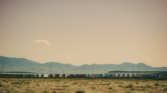 Specialized railcars transporting heavy industrial equipment through a rugged terrain under a clear blue sky.