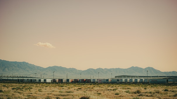 Specialized railcars transporting heavy industrial equipment through a rugged terrain under a clear blue sky.