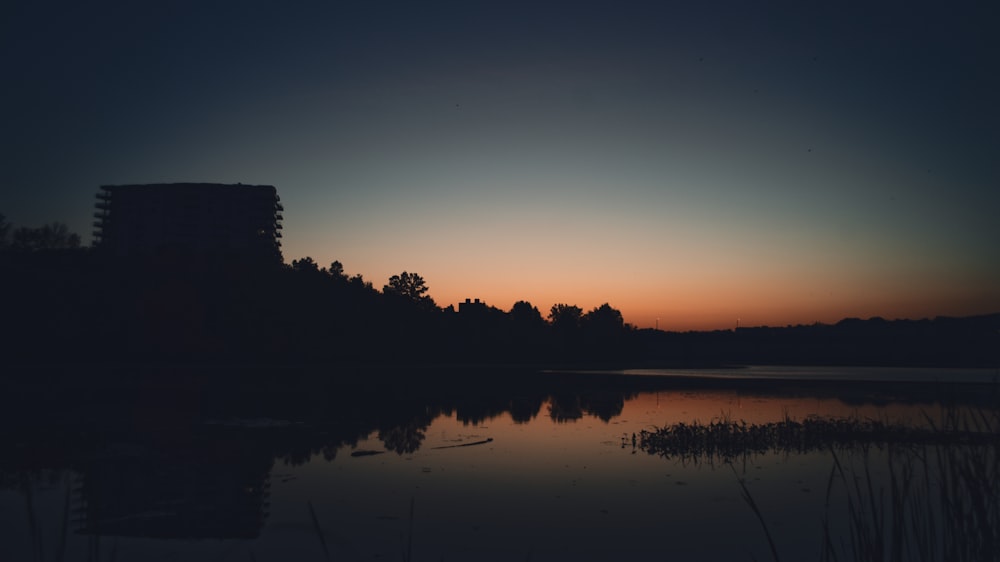 O sol está se pondo sobre um lago com um edifício ao fundo