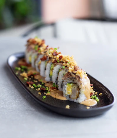 Close-up of a vibrant sushi roll with fresh avocado and salmon, artfully plated on a dark ceramic dish.