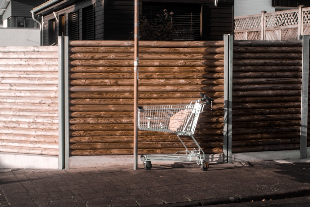 a shopping cart sitting in front of a wooden fence