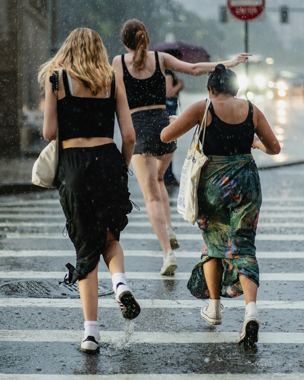 three women walking across a street in the rain