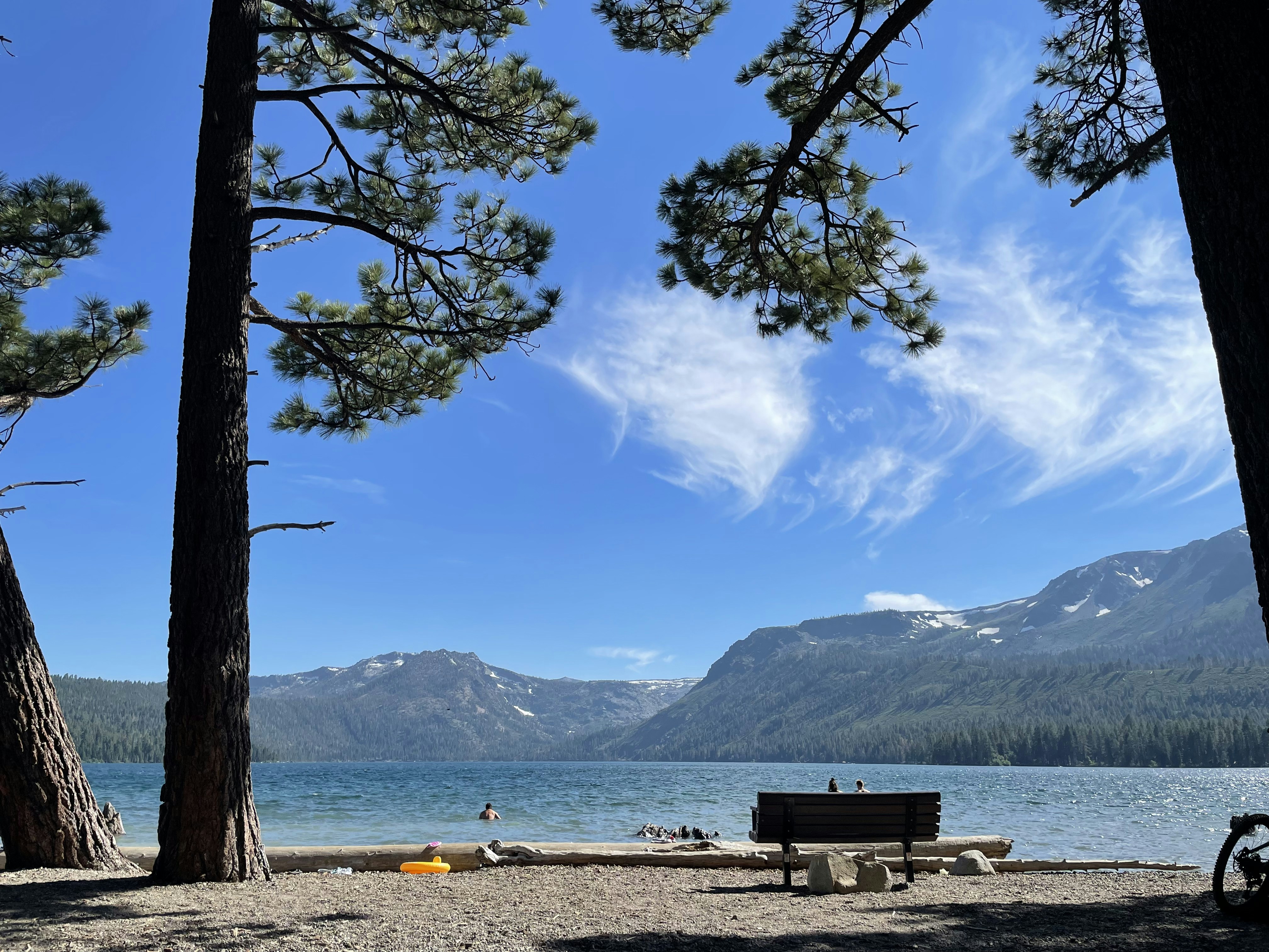 a bench on the shore of a lake with mountains in the background
