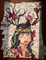 A collage depicting a woman's face made from various pieces of paper on a background of crumpled, printed sheets. Branches extend from her head with vibrant pink and red butterflies perched on them. The overall effect combines elements of nature and art in a visually engaging manner.