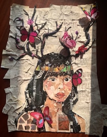 A collage depicting a woman's face made from various pieces of paper on a background of crumpled, printed sheets. Branches extend from her head with vibrant pink and red butterflies perched on them. The overall effect combines elements of nature and art in a visually engaging manner.