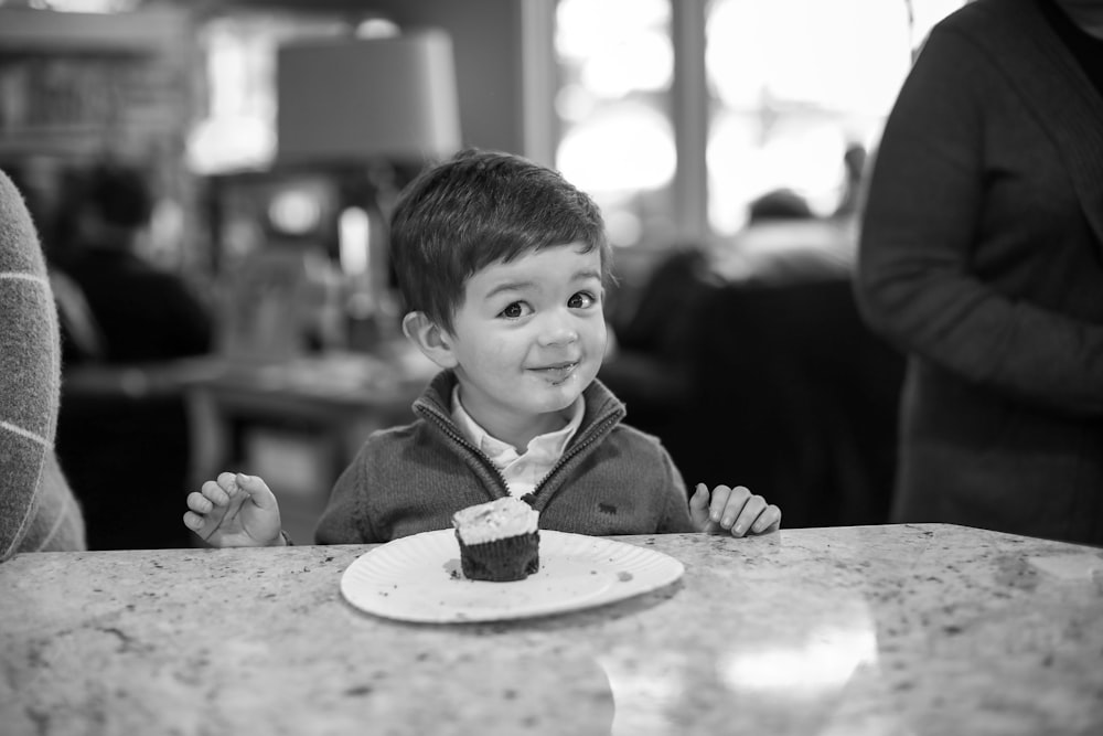 a little boy sitting at a table with a cupcake in front of him