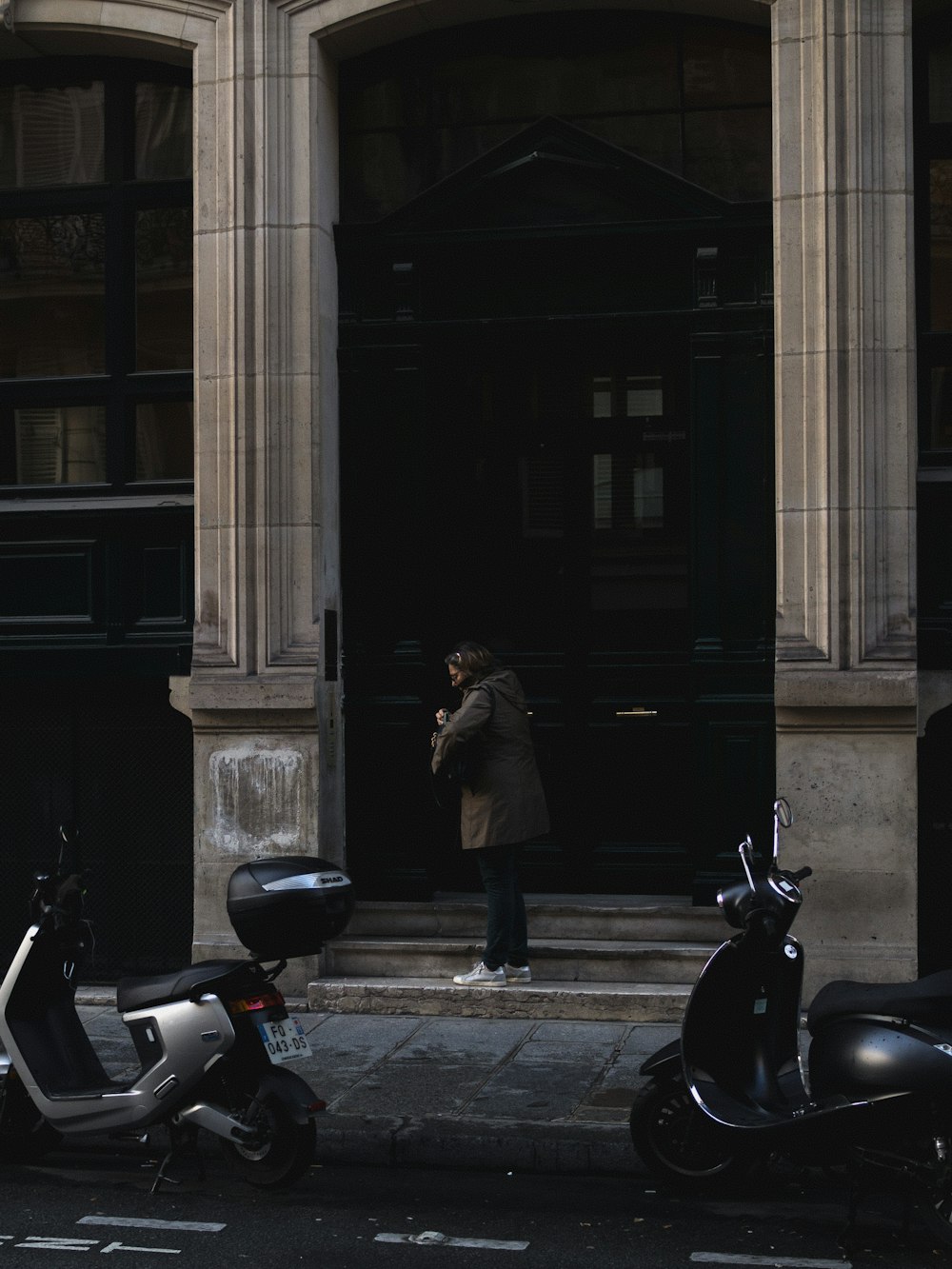 Un hombre parado frente a un edificio junto a scooters