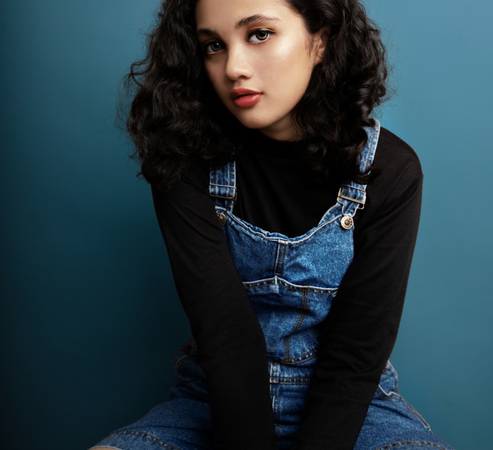 a woman sitting on a chair wearing overalls