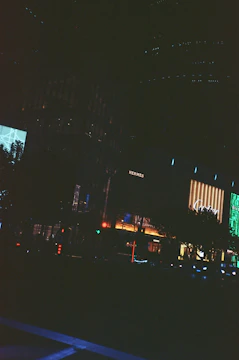 Dark urban night cityscape with subtle blue and silver lights reflecting a cinematic mood.