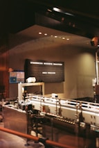 A dimly lit industrial-style interior featuring machinery and equipment. A black signboard displays the text 'Starbucks Reserve Roastery' and 'Honey Processed'. The setting suggests a specialized coffee processing area, with metallic pipes and a modern, sophisticated ambiance.