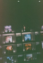 Several framed images and objects are arranged on illuminated shelves against a dark background. Some of the images include natural landscapes and artistic compositions, creating a curated and artistic display.
