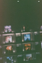 Several framed images and objects are arranged on illuminated shelves against a dark background. Some of the images include natural landscapes and artistic compositions, creating a curated and artistic display.
