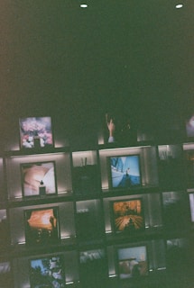 Several framed images and objects are arranged on illuminated shelves against a dark background. Some of the images include natural landscapes and artistic compositions, creating a curated and artistic display.